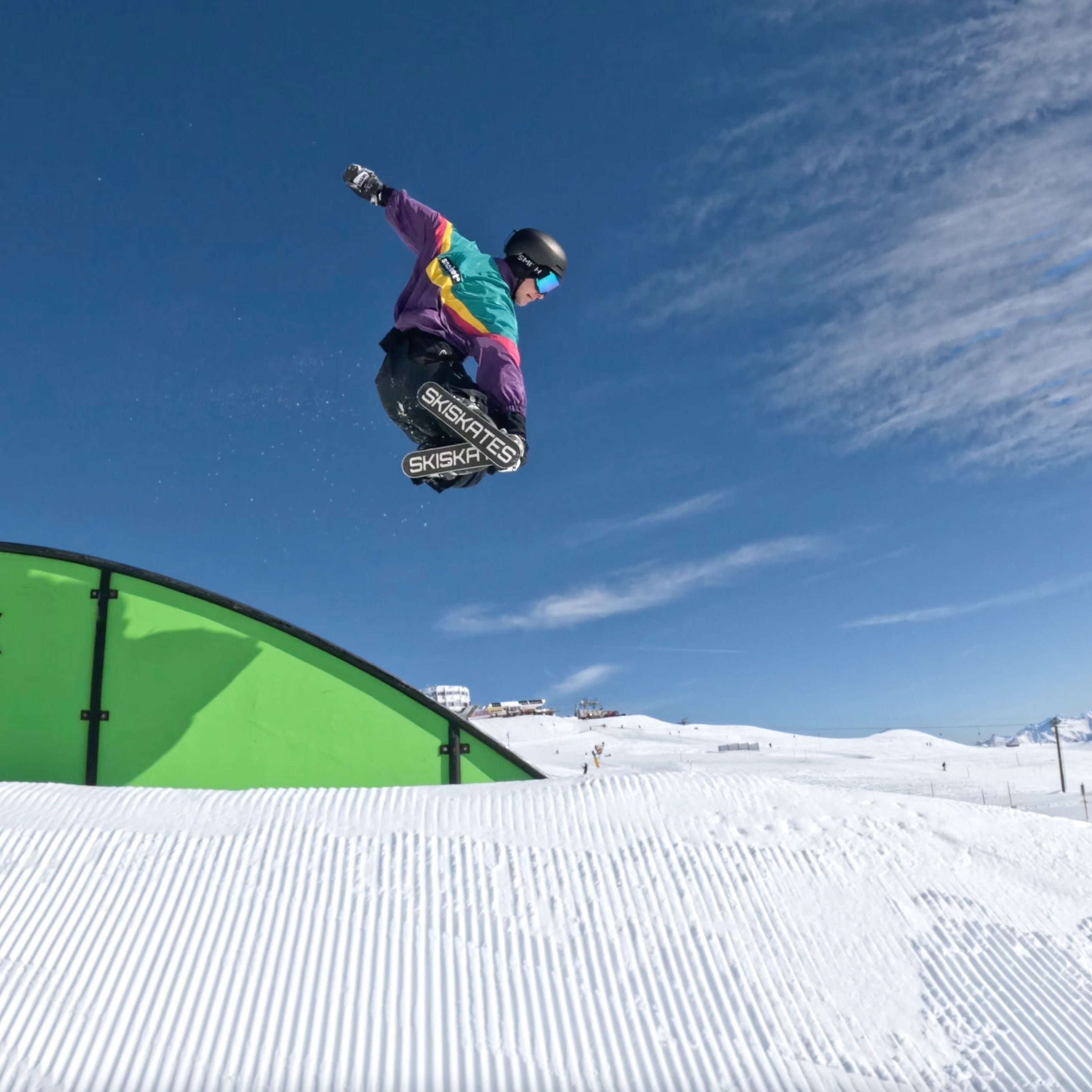 Person snowboarding off a ramp with against a blue sky and snowy landscape