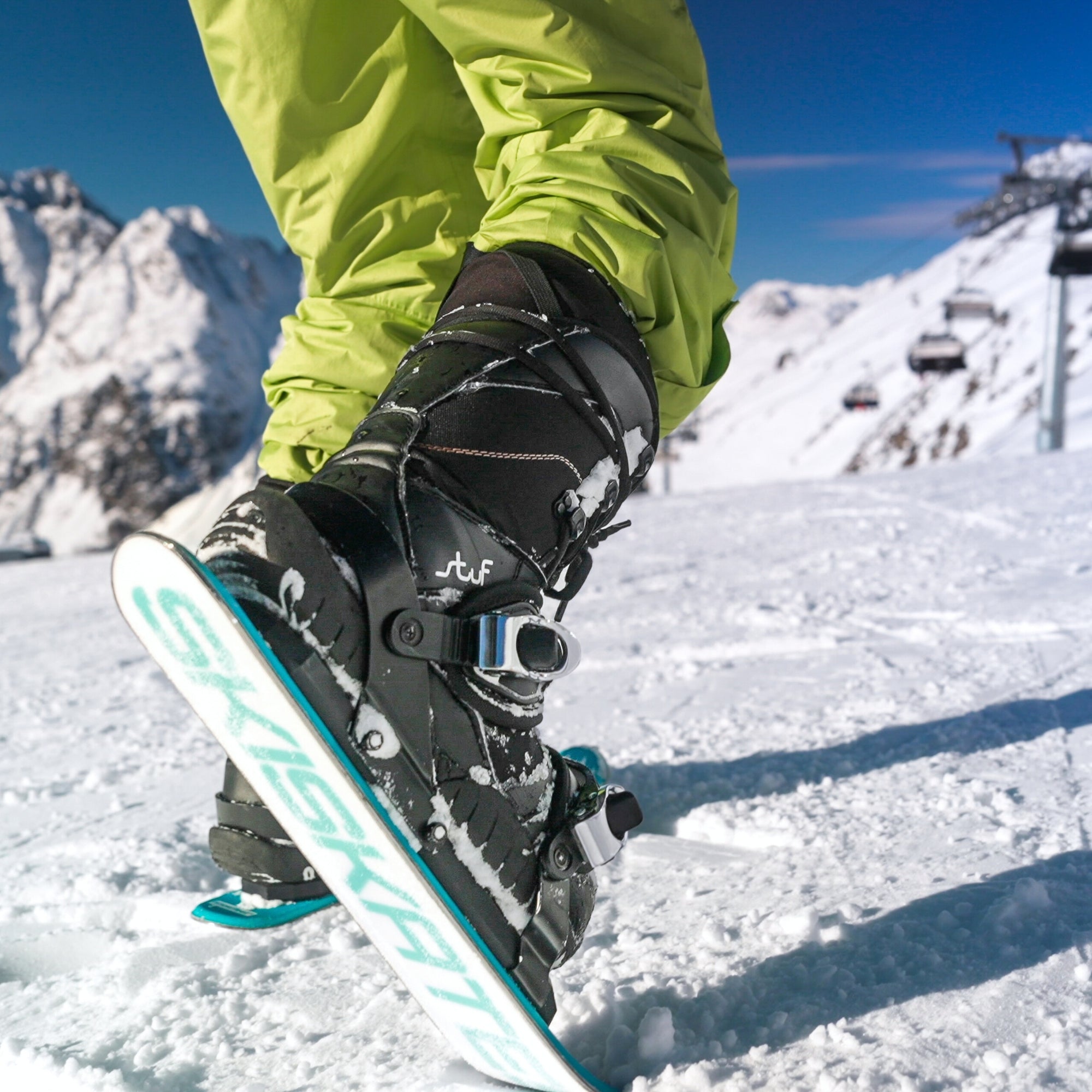 Person wearing a snowboard boot on a snowboard with a mountainous background