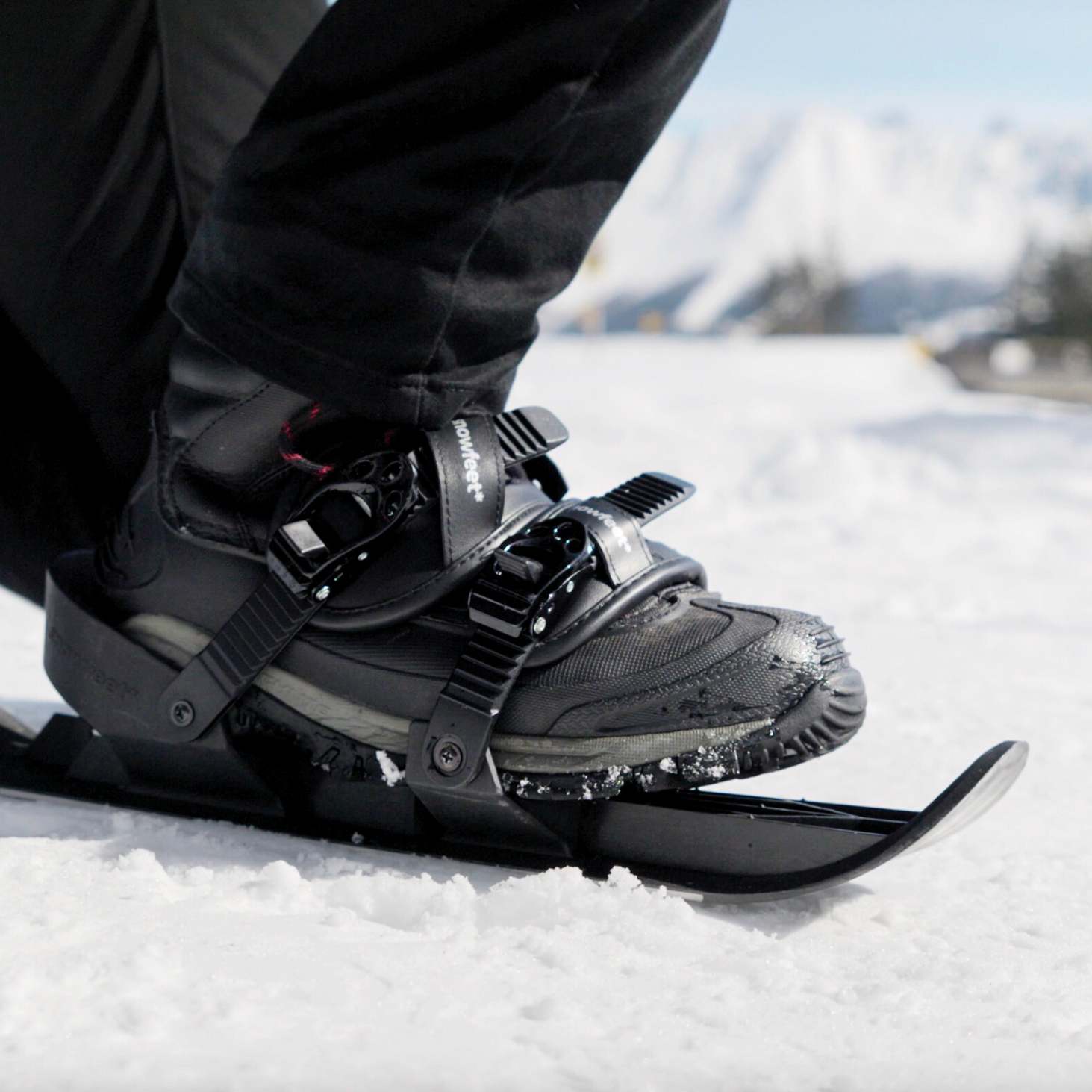 Person wearing snowshoe boots on a snowy ground with mountains in the background