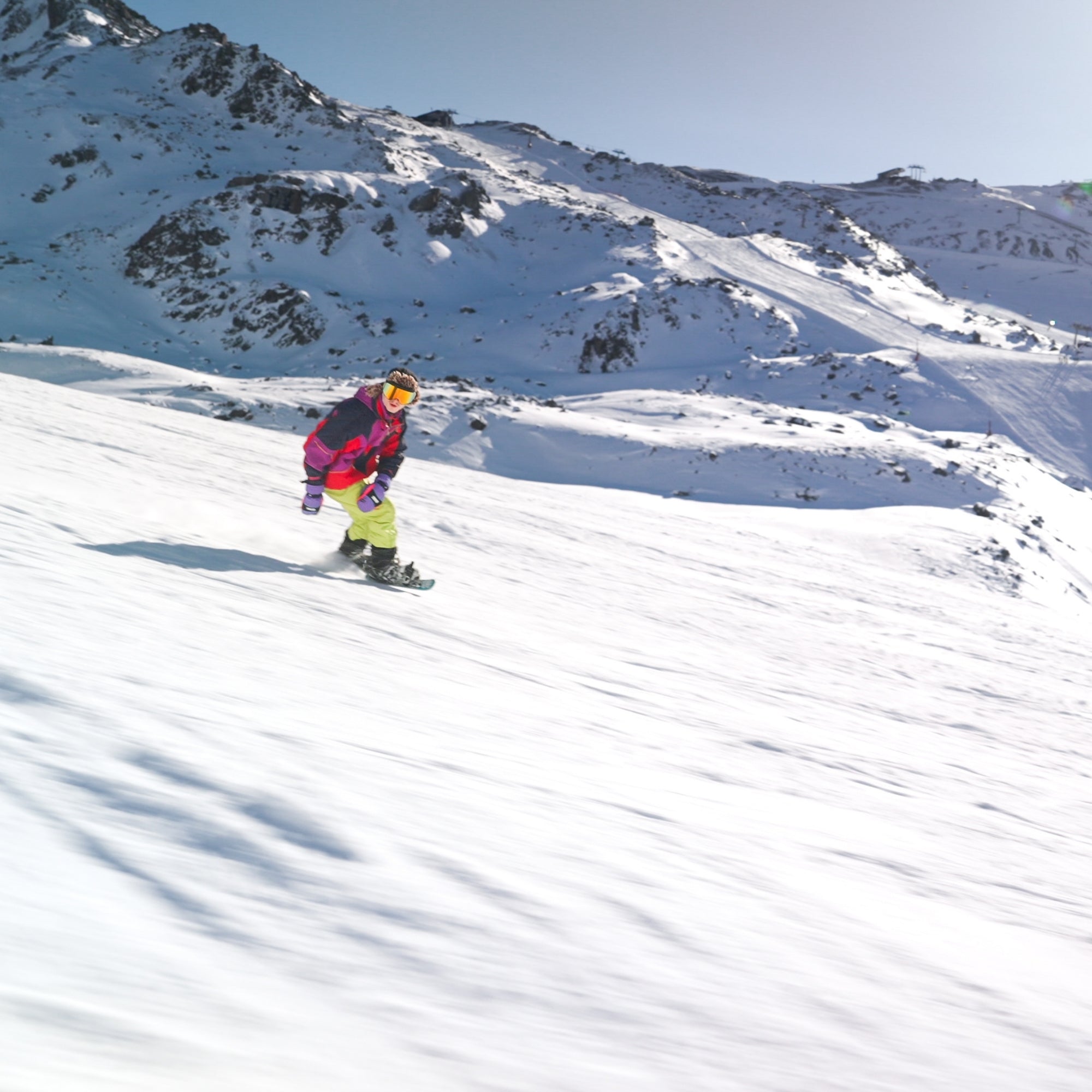 Person snowboarding down a snowy mountain slope with clear blue sky
